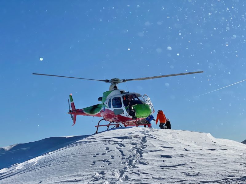 red, green and white helicopter on top of a snow capped mountain against a blue sky