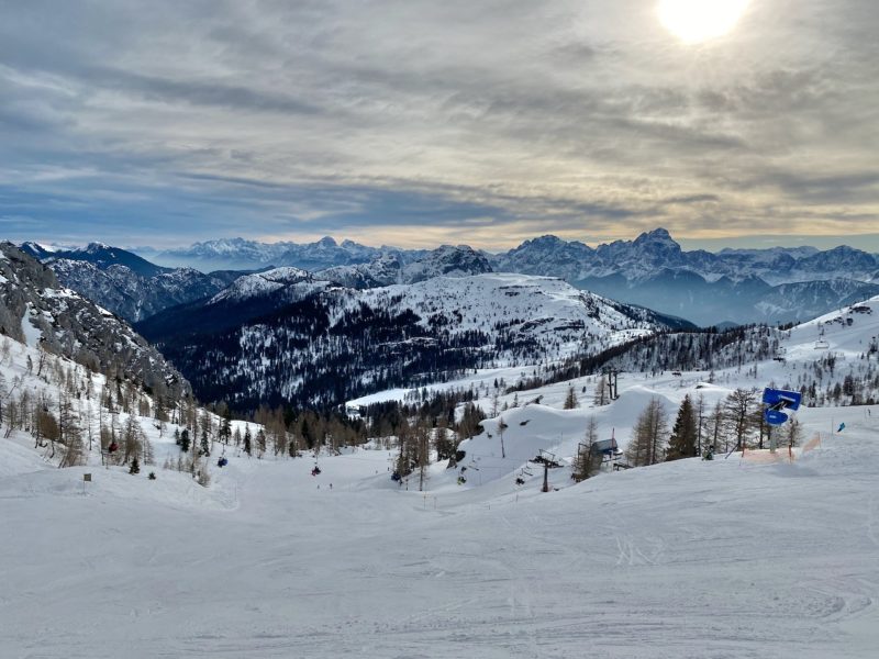 empty ski slope with panorama of mountains in distance cloudy sky with sun breaking through on right