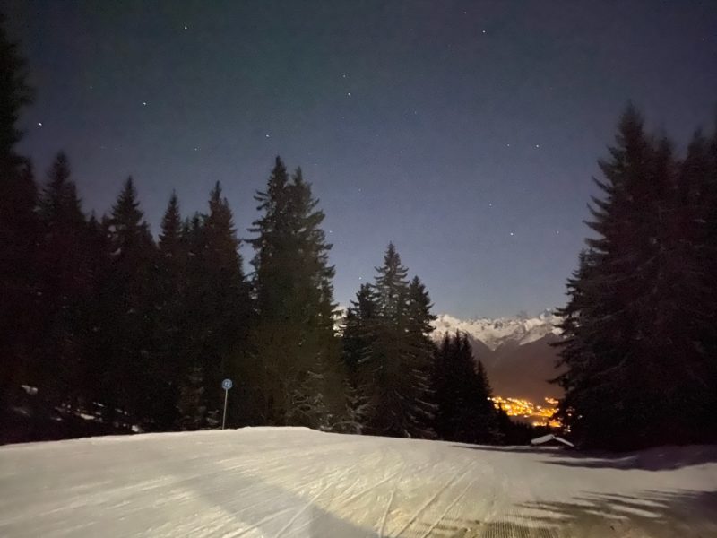 Ski slope surrounded by pine trees. slope is illuminated for night skiing