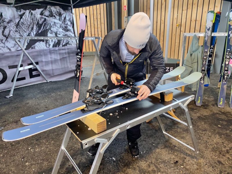 Man with screwdriver bending over a work bench setting the bindings of a pair of skis