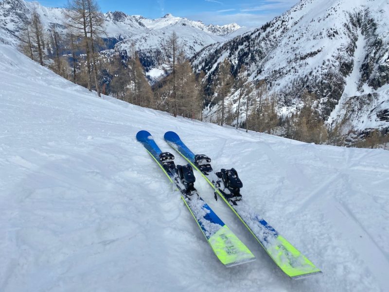 Bright blue skis with lime green tips, placed on the snow against a stunning mountainous backdrop