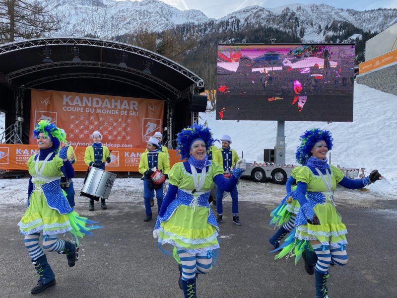 3 women dressed in blue striped tights and lime green and blue dresses dancing as part of the world cup slalom festivities