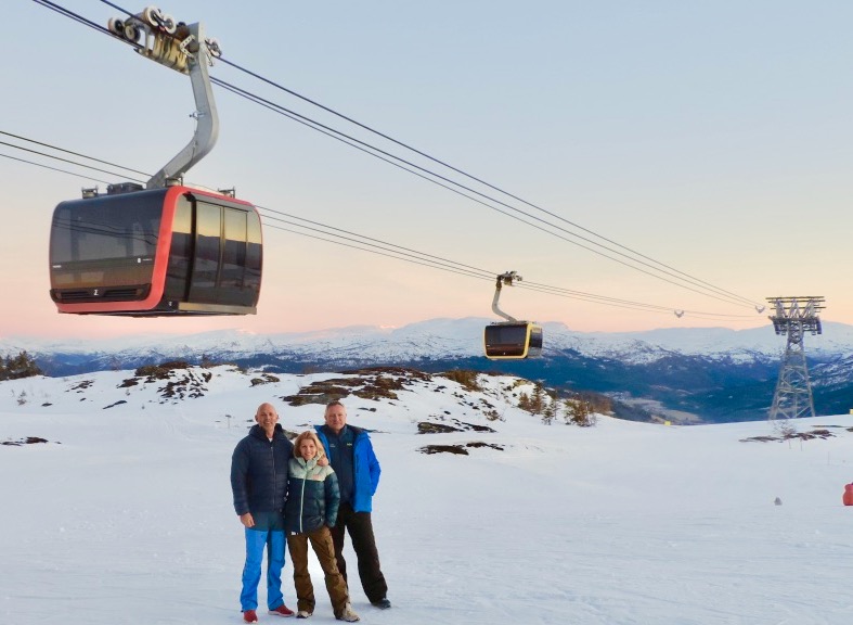 Snow scene, with cable cars overhead. Three people standing mid shot
