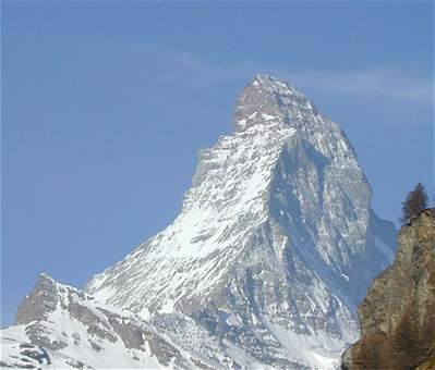 The iconic image of the Matterhorn wih a dusting of snow on two faces of the triangular mountain, wispy clouds in a dusty blue sky
